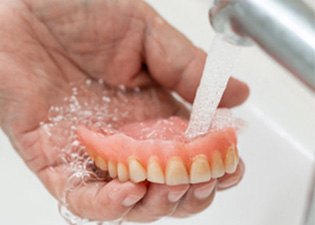 Person rinsing off their dentures  