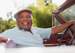 a smiling person with their hand on the wheel of an old car 