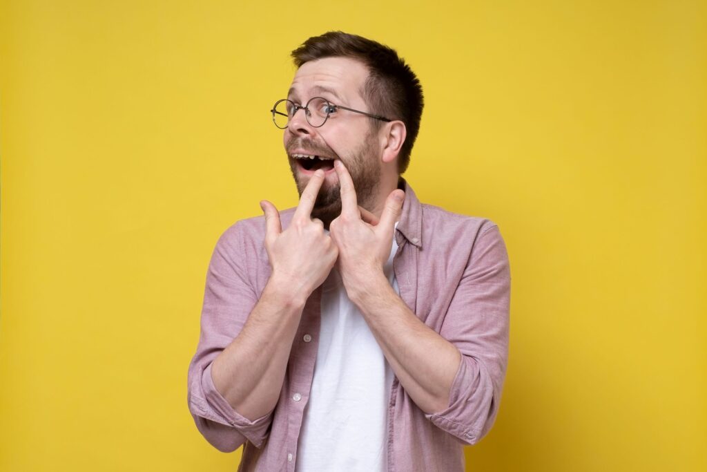 Man pointing to his missing tooth with two fingers in front of yellow background